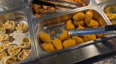 Kızarmış yengeç pençeleri ve bir self servis restoranında sıcak yemek dolu çelik tepsiler.