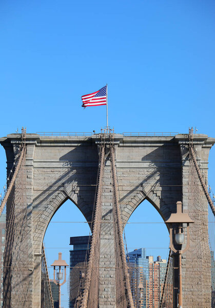 большой американский флаг, машущий над Бруклинской башней моста в Нью-Йорке и голубым небом на заднем плане