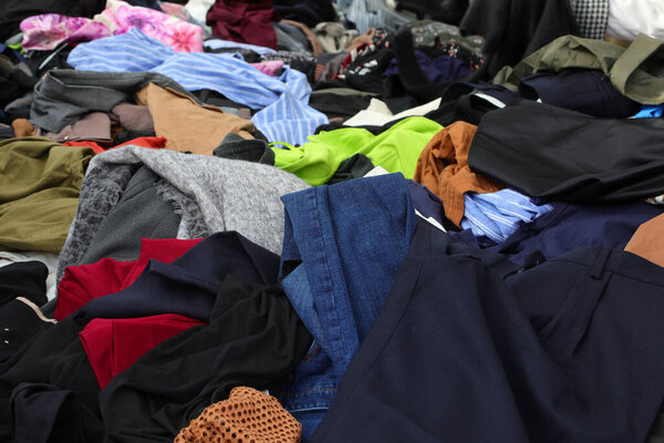 Messy pile of numerous used garments clothing and attire on an outdoor flea market stall