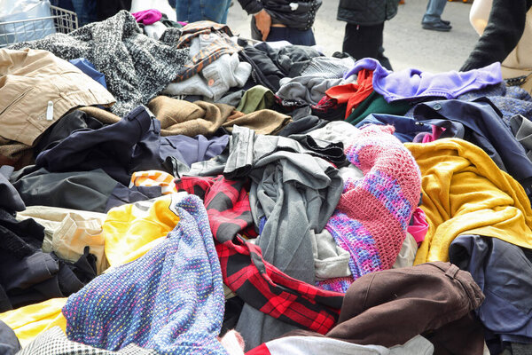 Messy pile of numerous used garments clothing and attire on an outdoor flea market stall