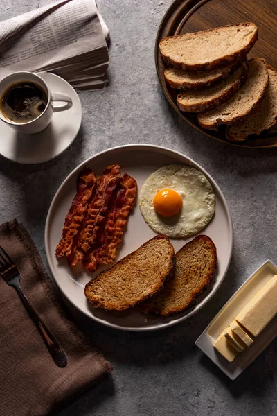 classic breakfast experience with this tantalizing photo featuring a delectable combination of crispy bacon, perfectly fried eggs, toasted bread, and a steaming cup of coffee
