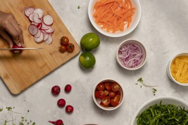 Sağlıklı bir yemek. Bir kadın, çeşitli salata malzemeleriyle çevrili ahşap bir masada taze bir turp dilimler.