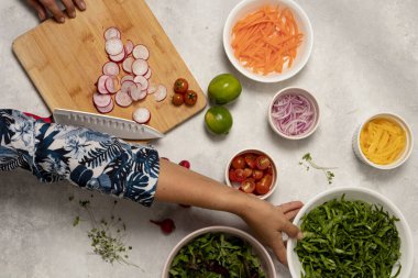 Sağlıklı bir yemek. Bir kadın, çeşitli salata malzemeleriyle çevrili ahşap bir masada taze bir turp dilimler.