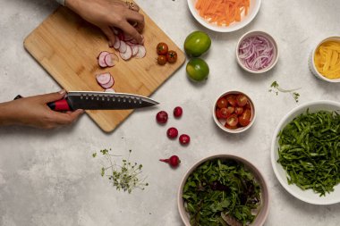 Sağlıklı bir yemek. Bir kadın, çeşitli salata malzemeleriyle çevrili ahşap bir masada taze bir turp dilimler.