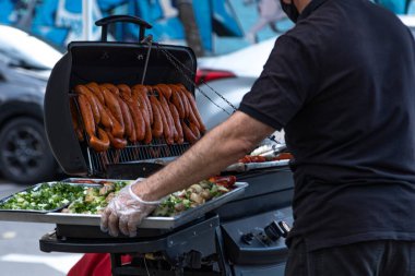 Bu canlı görüntüde şehir yemeklerinin keyfini yaşayın. Bir adam güneşin sıcacık ışıltısı altında salata pişiriyor ve mutfak macerasına bir parça rahatlama katıyor.