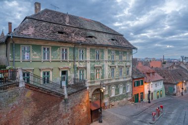 Eski hanın kasvetli manzarası Zur Ungarische Krone 'nin günbatımında bulutlu bir gökyüzünün altında, yumuşak bir ışıkla yakalanması tarihi perenin detaylarını vurguluyor..
