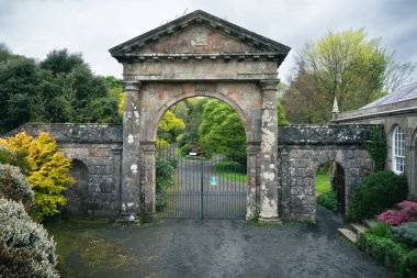 Kuzey İrlanda 'daki Mussenden Tapınağı ve Demesne Tepesi' nin giriş kapısı, bulutlu bir sonbahar gününde, tarihi mekanı çevreleyen sıcak sonbahar yeşillikleriyle birlikte ele geçirildi..