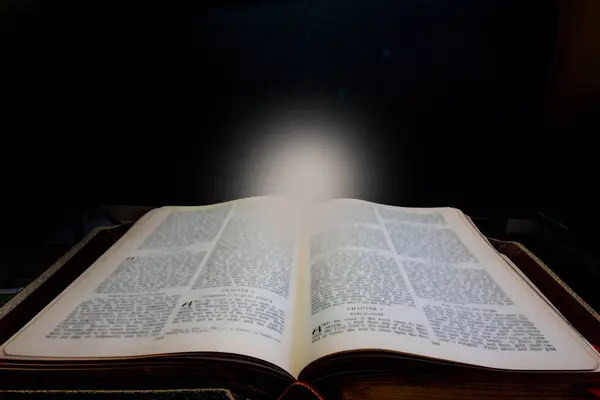 Very old book leads to a source of light against a black background