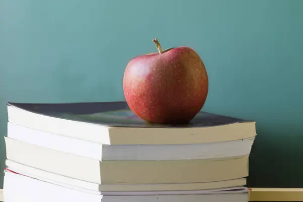 赤いりんごは背景にチャックボードが付いている本の積み重ねの上に座ります ロイヤリティフリーのストック画像
