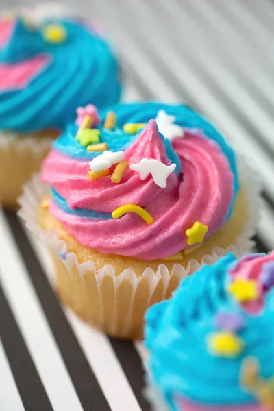 黒と白の裏地の背景に青とピンクのアイシングの行にカップケーキ — ストック写真