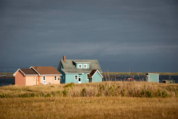 海边五颜六色的蓝绿色和桃色的房子 位于加拿大魁北克省麦哲伦岛上的哈弗尔 奥伯特的成本线被破坏 前景一片灰蒙蒙的天空和黄色的草地 — 图库照片