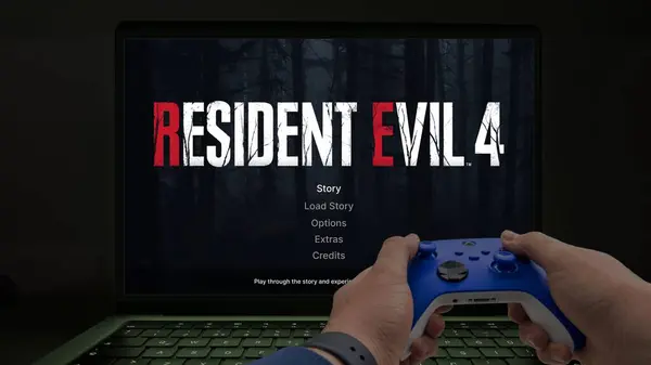 İstanbul, Türkiye - 27 Şubat 2024: Mavi bir xbox kontrolörüyle Macbook bilgisayarında Resident Evil 4 'ün yeniden çevrimini oynamak. Capcom tarafından Playstation, Xbox, PC, Mac ve iOS için oynanan bir oyundur.