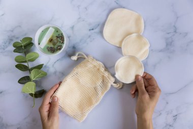 Üzerinde yeniden kullanılabilir pamuk pedleri olan bir çanta mermer arka planda makyaj çıkarıcıları.