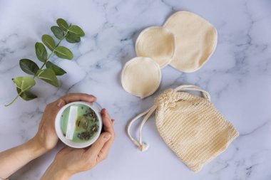 Üzerinde yeniden kullanılabilir pamuk pedleri olan bir çanta mermer arka planda makyaj çıkarıcıları.