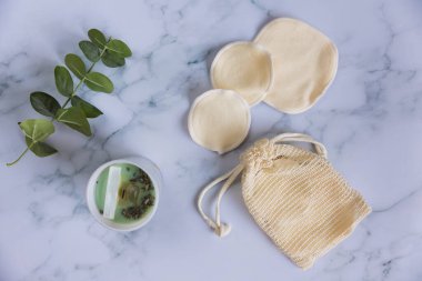 Üzerinde yeniden kullanılabilir pamuk pedleri olan bir çanta mermer arka planda makyaj çıkarıcıları.