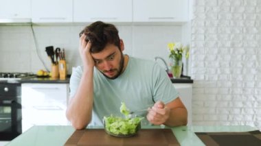 Üzgün genç bir adam salataya özlemle bakar elinde yeşil bir çatal ve önünde bir tabak salata ile. Yorucu bir diyet, sağlıklı yiyeceklerden nefret eder. Diyet yapma.