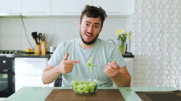 一个年轻的节食者把食指指向面前的一碗沙拉 这应该是吃绿色沙拉健康食品的概念吗 坐在他的厨房里看着相机 — 图库视频影像