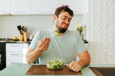 Önden bakıldığında, elinde tuttuğu salata çatalına ve kâseye sırtını dönmüş mutlu bir genç adam değil. Lezzetli yeşil yaprak salatası. Diyet yapma.