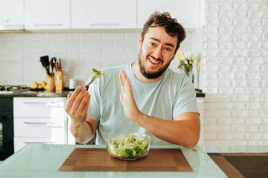Genç adam artık yeşil salatasını yemek istemiyor, yorgun. Adam diyet yemek için yanıp tutuşuyor. Sağlığımızı geliştirmemiz gerekiyor. Sağlıklı gıda konsepti. Diyet yapma.
