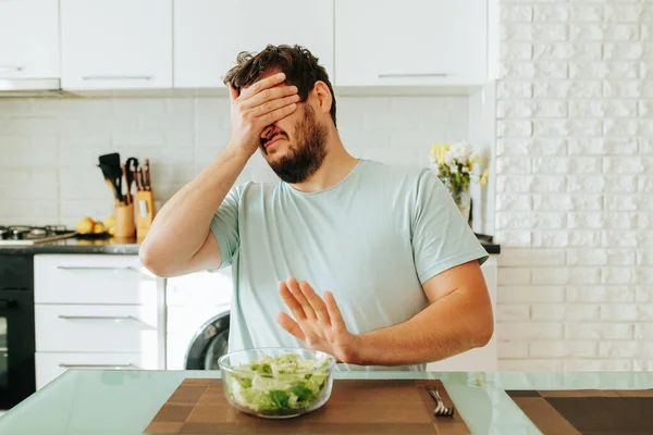 The young man put out one hand in protest, and the other closed his eyes, showing that he did not want a salad. It is hard to go on a diet when you love delicious food. Front view. Stop diet.
