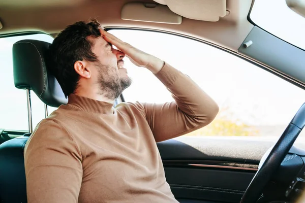 stock image A terrible grimace of pain on the face of a young male driver, a hand on his forehead, a grimace on his face. Headache often haunts drivers. Hard work. Emotions and people.