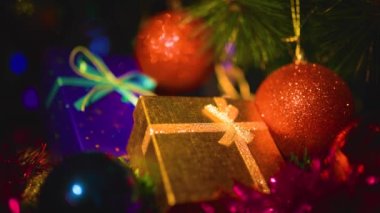 Kırmızı parlak Noel toplarını altın ve mavi hediye kutularının yanına kapat. Çelenklerin ışıltısı bayram duygusunu arttırır. Herkes hediyeleri bekliyor. Seçici odak.