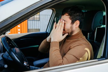 Yorgun genç bir adam ellerini yüzüne yakın tutar gözleri kapalı ve dinlenir. Yorgun, bunalımlı, dinlenmek için durmuş. Sürücüler dinlenme konsepti.