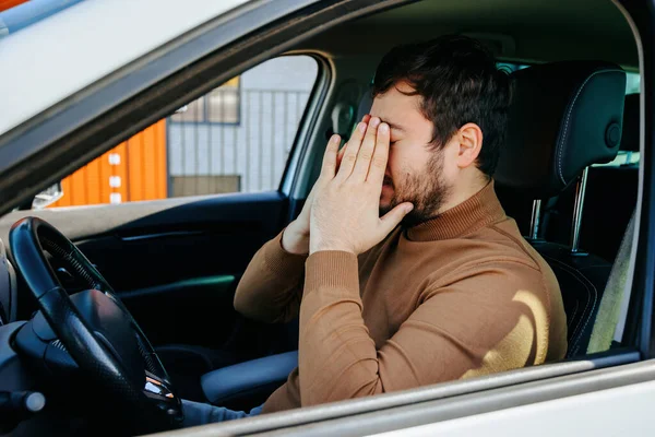Yorgun genç bir adam ellerini yüzüne yakın tutar gözleri kapalı ve dinlenir. Yorgun, bunalımlı, dinlenmek için durmuş. Sürücüler dinlenme konsepti.