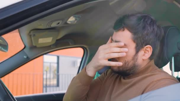一个筋疲力尽的年轻人坐在车里的司机座位上揉揉眼睛 累了一天的工作 休息在车上 胡子和疲倦的样子 — 图库视频影像