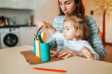 Neşeli, sevimli bir anne ve küçük kız evlerinde masada oturuyor ve yerlerine renkli oyuncak çubukları yerleştiriyorlar. Dadı, eğitimci çocuğu eğlendirir, öğrenme oyununu sever. Bulanık.