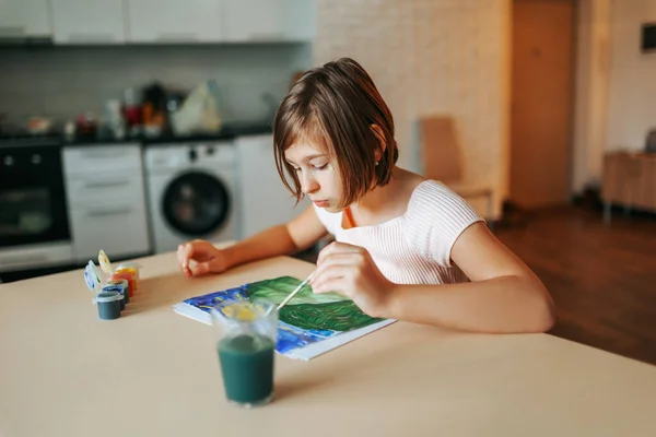 Beautiful girl enthusiastically draws her drawing with paints, confidently hold brush with left hand. Left handed child draws beautifully. Hobbies you do at home.