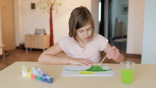 一个漂亮而严肃的小女孩坐在书桌前 用左手在相册里画了些什么 她正专注于工作 可爱的孩子在做他喜欢的事头发被射中 — 图库视频影像