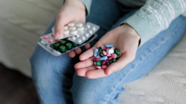 Tanınmayan kişi evdeki kanepede oturuyor ve elinde bir sürü farklı renkte hap tutuyor. Bazı haplar su toplamış. Eczacılık firması. Yaşam biçimi.