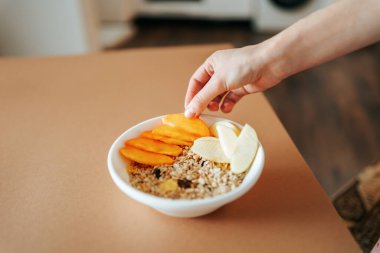 Yulaf lapası ve meyveli en üst tabakta, tanınmayan kadın eli meyve koyuyor. Sağlıklı yemek, sağlıklı kahvaltı..