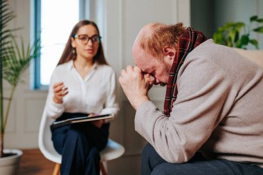 Profesyonel psikiyatrist ve erkek hasta ofiste istişarede bulunuyorlar, dikkatle dinleyen ve not alan genç bir bayan. Psikoterapi konsepti, doktor reçetesi, müşteri güveni,