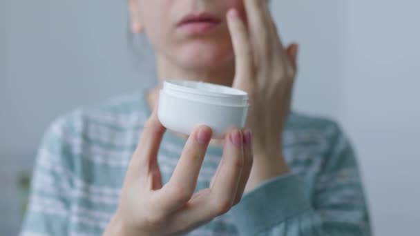顔のクリームの女性の手瓶の中に保持優しく肌を栄養化し 保湿するために彼女の顔にクリームローションを適用します 女性性 ライフスタイルの概念 スキンケア 指でクリームを適用します 女性の毎日の治療 — ストック動画