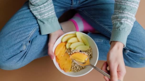 認識できない人は彼のアパートの床に座って 手に健康的な朝食とスプーンとプレートを保持しています 健康志向の人の手の中に健康的な朝食 植物性食品 — ストック動画