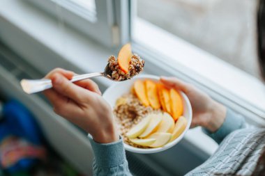 Close up of hands of woman holding a spoon and homemade granola in a plate natural ingredients. Focus on a spoon with fruit and grain. Dieting, nutritionist, healthy food, modern food, pieces fruits.