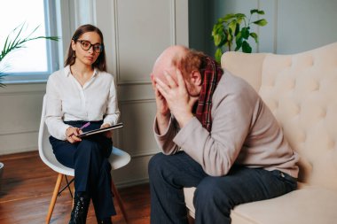 Worried elderly man patient sitting at a psychologists therapist appointment and telling about mental problems, woman psychologist consulting sad European man, people displeased, human unhappy,
