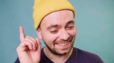 guy Smiling laughing and Making Attention Sign with a Finger Gestures and looking at camera, he points his finger at the camera, studio shot on the blue background, man with yellow hat