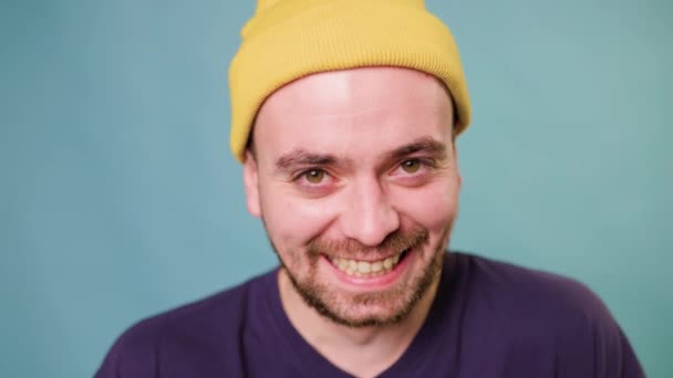 滑稽的 疯狂的 快乐的人类情感 兴奋的家伙在蓝色的背景下微笑 看着相机笑着 戴着黄色帽子的快乐休闲嬉皮士 — 图库视频影像
