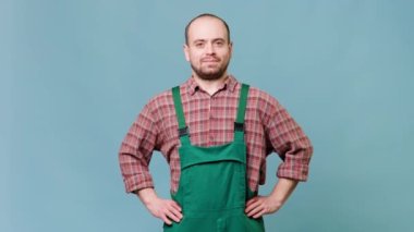 portrait of a content bearded workman looking at camera and arms on hips. Check out this beautiful studio shot of a happy young worker in overalls. Perfect for advertising campaigns