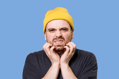 guy in the studio portrait seems to be suffering as he looks directly at the camera with a worried expression, with the studio shot, stressed male face looking at camera in blue background studio