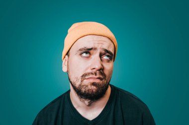 close up portrait of a Exhausted young bearded brunette male and looking tiredly, wearing casual clothes while posing over blue background. studio shot,