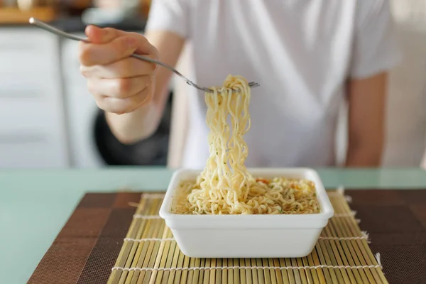 A close up shot of a fork in the hands of someone at home, savoring a steaming plate of showing instant noodles.
