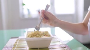 A close up shot of hand a quick and unhealthy meal of fast food, showing instant noodles, with the focus on the fork in their hand.