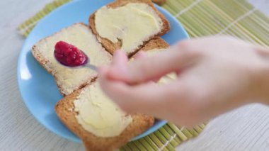 The hands of someone add jam on the butter on bread, showing the care and attention to detail put into making a healthy meal.