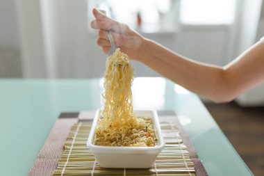 A imagine of a fork in the hands of someone indulging in junk food, with the kitchen in the background. using a fork to enjoy a plate of unhealthy pasta.