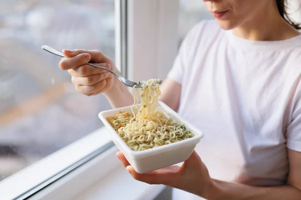 A candid shot of someone enjoying a junk food meal of instant noodles, focuses on the hands and fork, showing the consumption of the unhealthy meal.