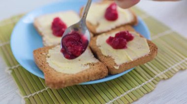 A shot of a persons hands preparing add jam on the toasted bread with butter, emphasizing the simplicity of a healthy breakfast.